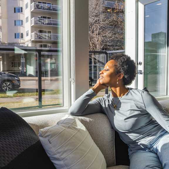 a woman is sitting on a couch looking out a window.