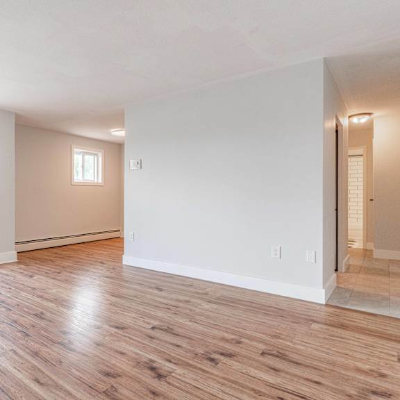 a spacious room with wooden flooring and white walls.