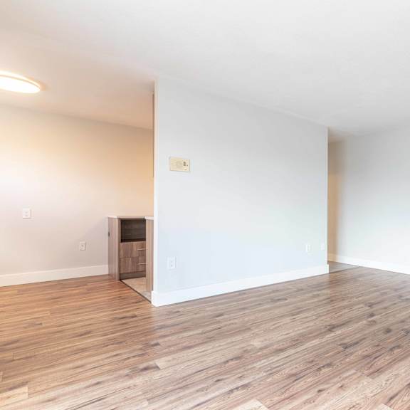 a room with wooden flooring and a white wall with a door in the corner.