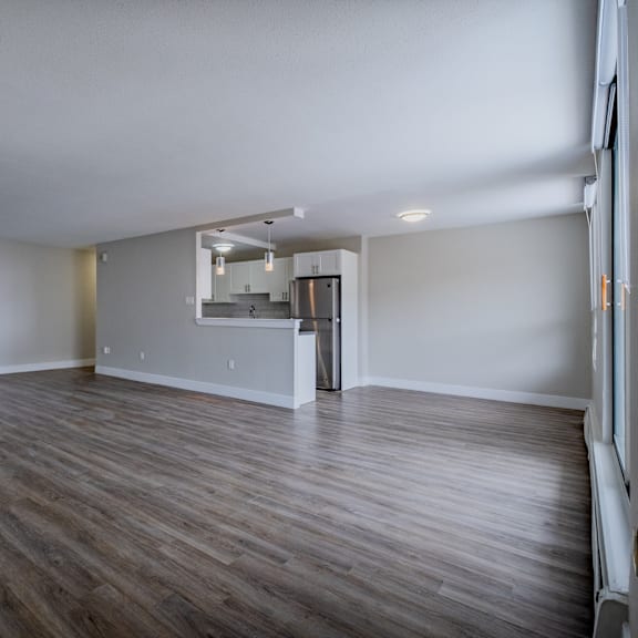a spacious room with wooden flooring and a kitchen area in the background.
