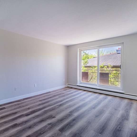 a room with wooden flooring and a window overlooking a backyard.