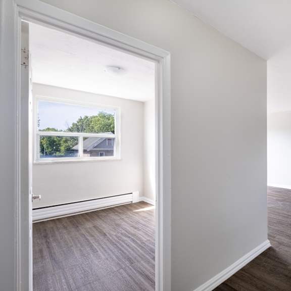 a room with white walls and wooden flooring with a doorway leading to another room.