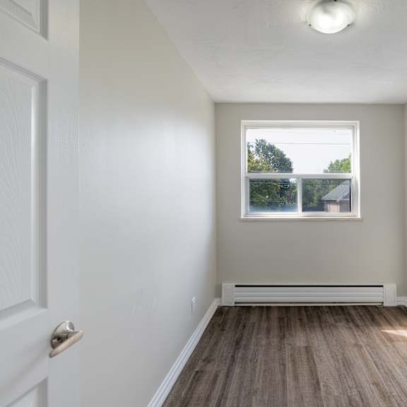 a white door opens to a room with a window and a wooden floor.