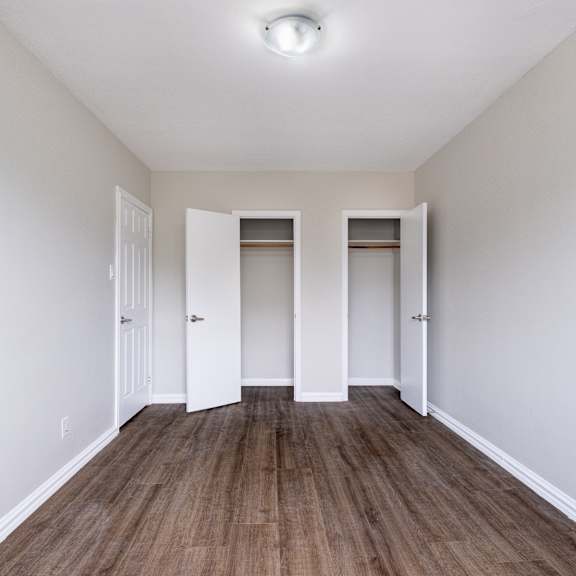 a room with white walls and wood flooring with three white doors.