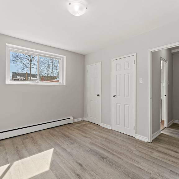 a room with a window, white walls, and a wooden floor.