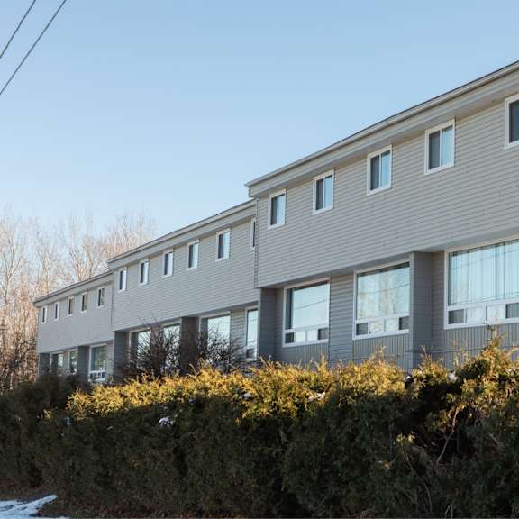 a building with grey siding and white trim is surrounded by a hedge.