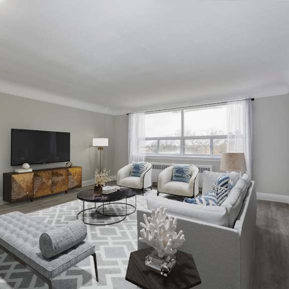 a living room with a grey couch, a grey ottoman, a black television, and a wooden side table.