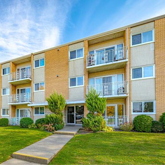 a row of apartment buildings with balconies and green lawns in front.