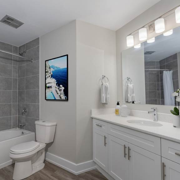 a bathroom with a white toilet, a white sink, and a painting of a beach scene on the wall.