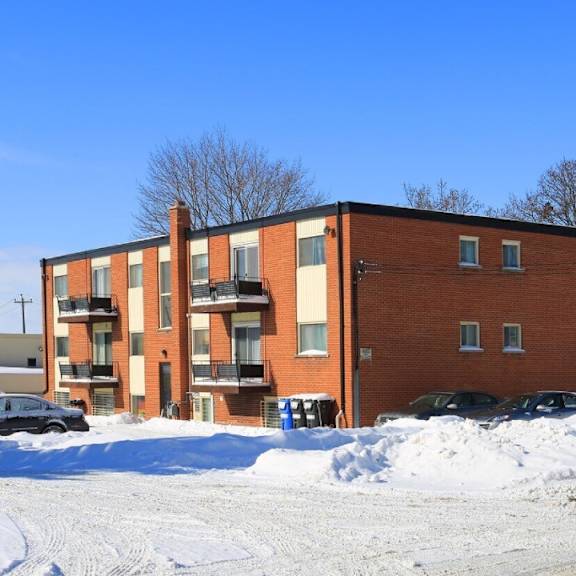 a red brick apartment building with snow on the ground and cars parked in front.