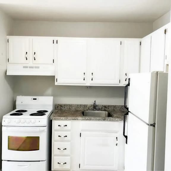 a white kitchen with a stove, sink, and refrigerator.