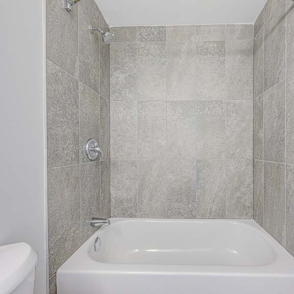 a white bathtub sits in a bathroom with grey tiles.