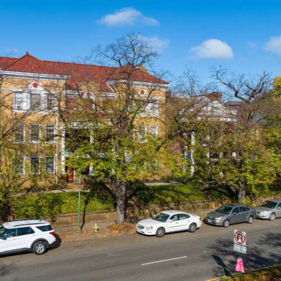 a red-roofed building is surrounded by trees and cars are parked on the street.