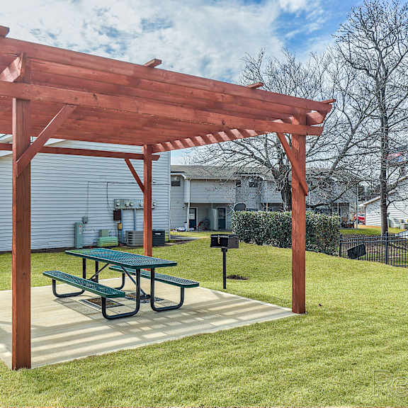 a wooden pergola with a green table is in the middle of a grassy area.
