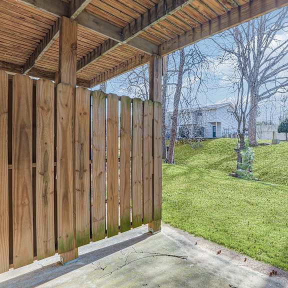 a wooden deck with a view of a grassy lawn and a white house.