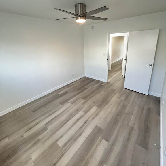 a room with a ceiling fan and light, and a doorway leading to another room.