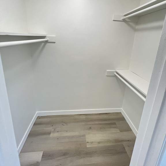 a white closet with shelves and a wooden floor.