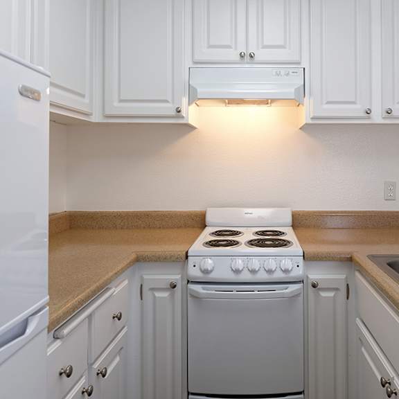 a white kitchen with a stove, sink, and cabinets.