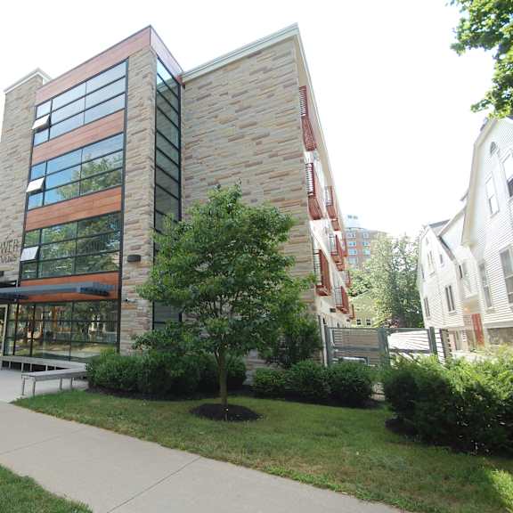 a modern building with a glass facade is surrounded by greenery and a sidewalk.