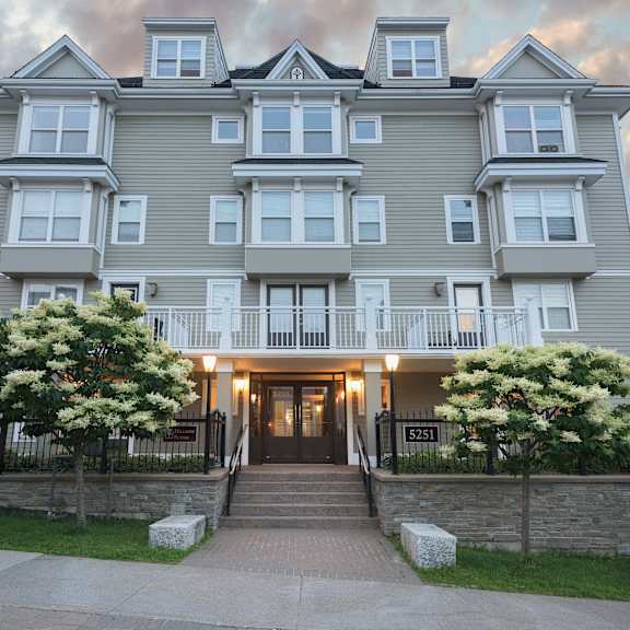 a large grey apartment building with a black fence and a stone wall in front.