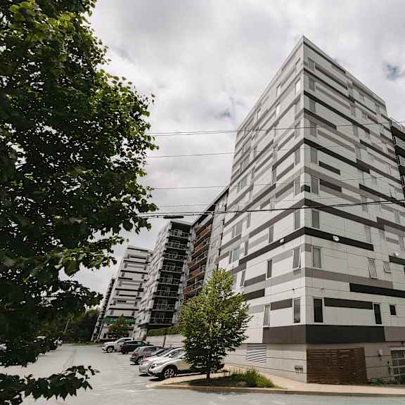 a tall building with a modern design is surrounded by a parking lot and trees.