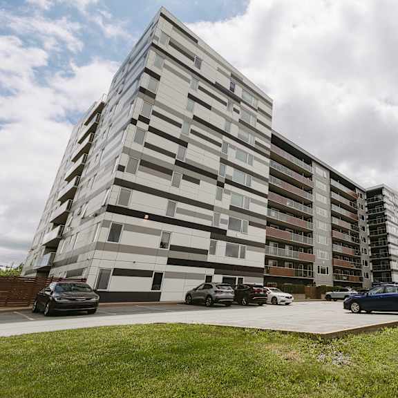 a modern building with a grassy area in front and cars parked along the side.