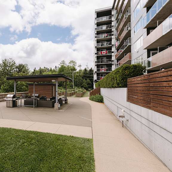 a modern outdoor seating area with a picnic table and chairs is surrounded by a grassy lawn and a tall building.