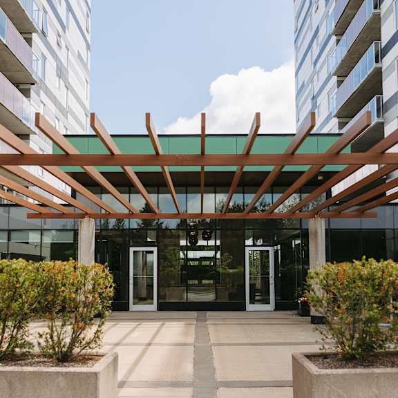 a modern building entrance with a wooden pergola and concrete planters.