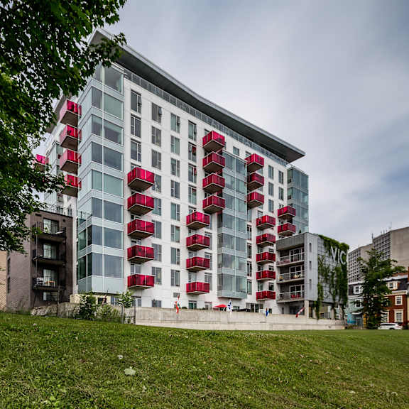 a modern building with red balconies is surrounded by greenery.