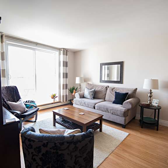 a living room with a grey couch, a black chair, a wooden table, and a painting on the wall.