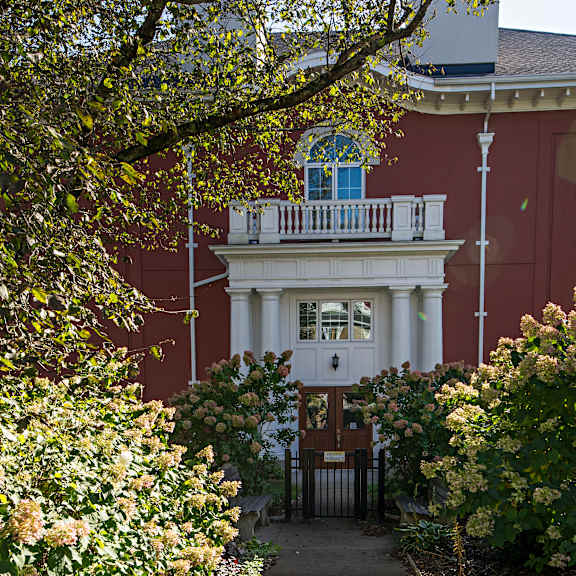 a white building with a balcony is surrounded by green plants.