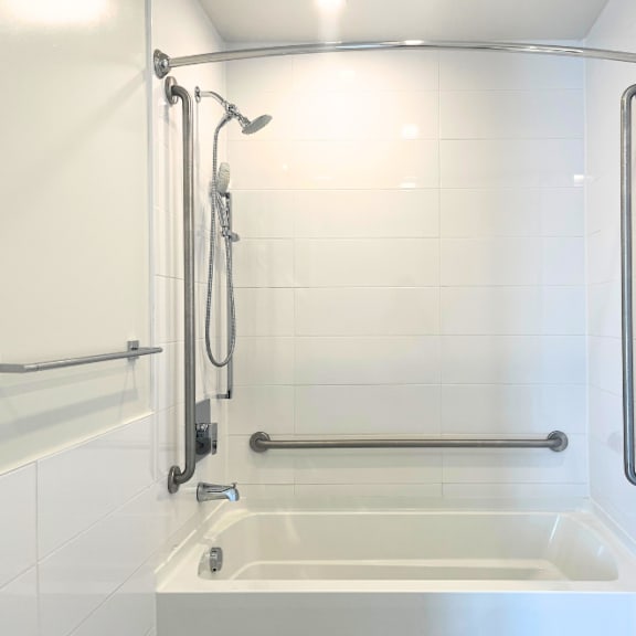 a white tiled bathroom with a glass shower door and a glass shower head.