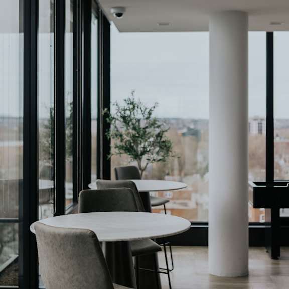 a modern cafe with white tables and chairs and large windows.