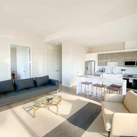 a modern living room with a grey sofa, a beige armchair, and a glass coffee table.