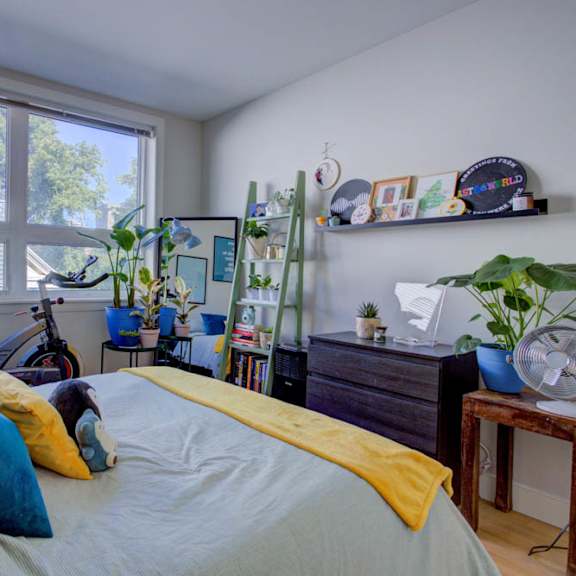 a bedroom with a bed, a bicycle, a fan, and a window with blinds.