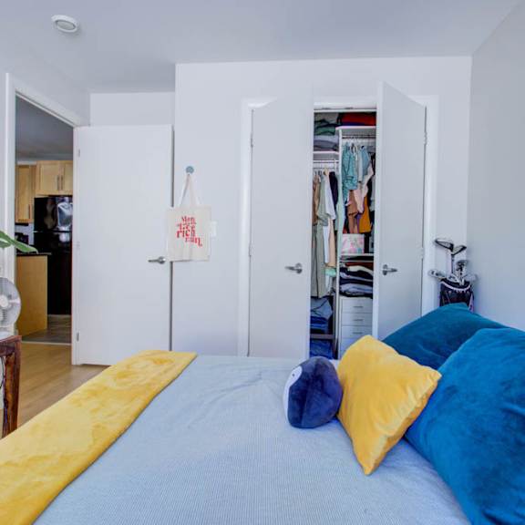a bed with a yellow blanket and blue pillows is in the foreground of a room.