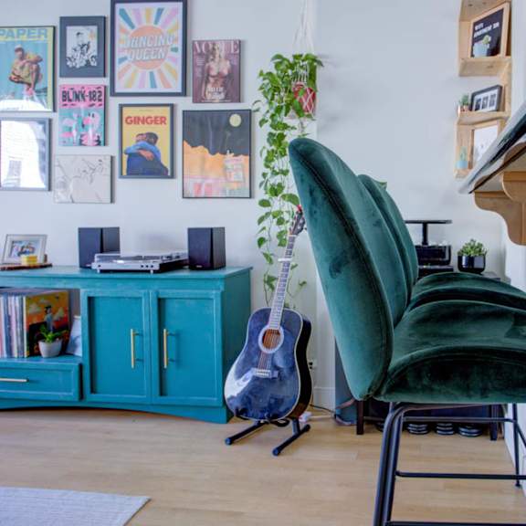 a green chair sits in front of a wooden desk with a guitar leaning against the wall.