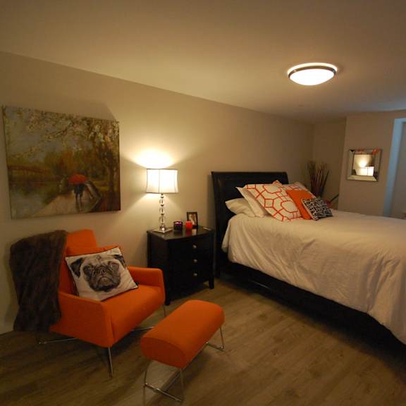 a bedroom with a bed, nightstand, chair, and painting on the wall.