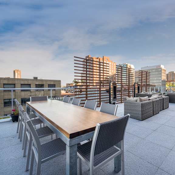 a rooftop patio with a long table and chairs overlooking a city skyline.
