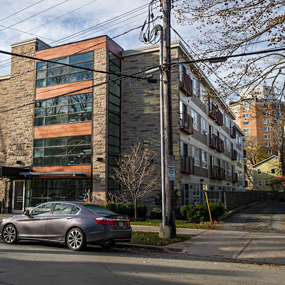 a modern building with a glass facade is surrounded by other buildings and parked cars.