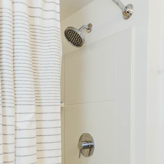 a white shower curtain is hanging in a white tiled shower.