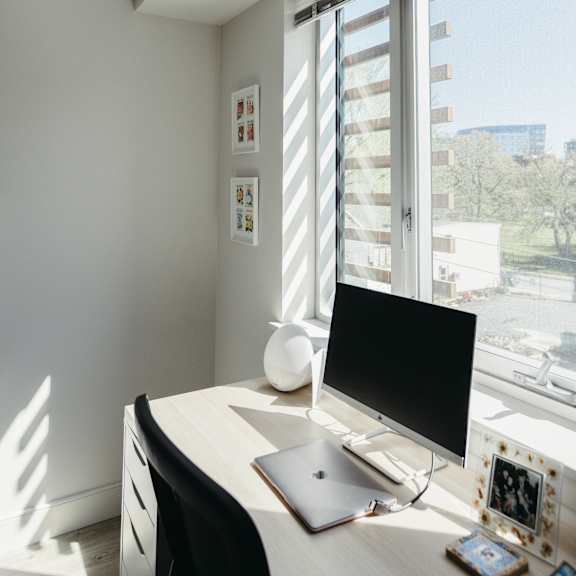 a laptop and a monitor on a desk with a window behind it.