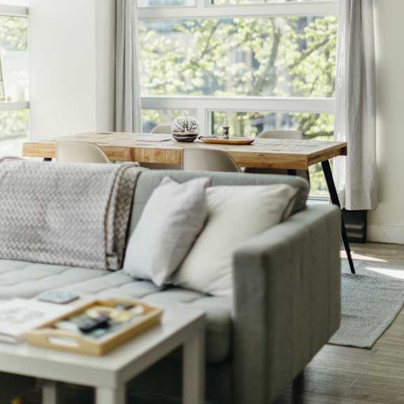 a grey couch with a coffee table in front of a window with a view of trees.