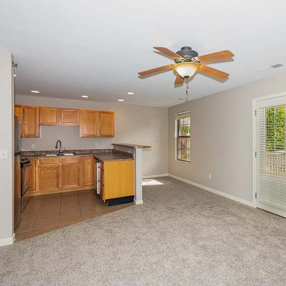 a room with a ceiling fan and a kitchen area with wooden cabinets.