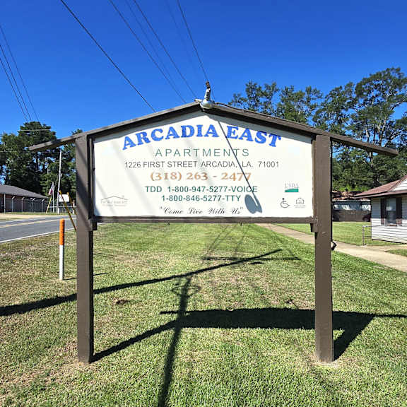 a sign for arcadia east apartments is displayed in front of a grassy area.