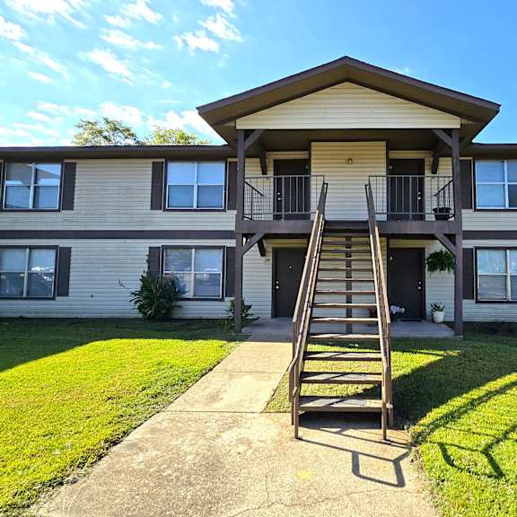 a two-story apartment building with a balcony and a staircase leading to the entrance.