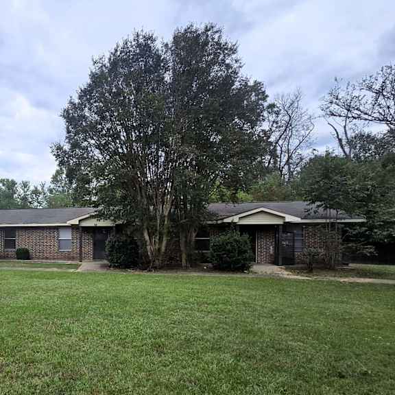a house with a green lawn and trees in front.