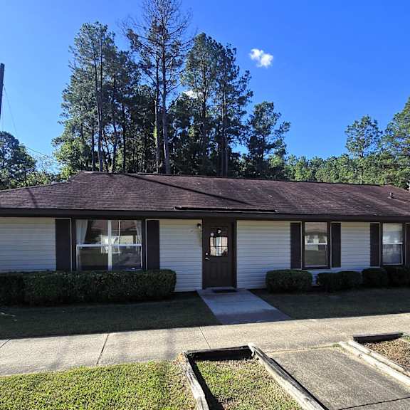a house with a brown roof and white siding is surrounded by greenery and a clear blue sky.