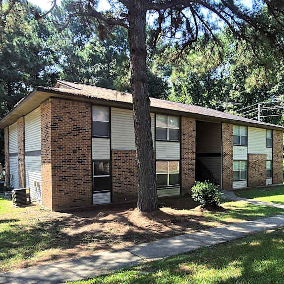 a house with a brown brick exterior and a tree in front.