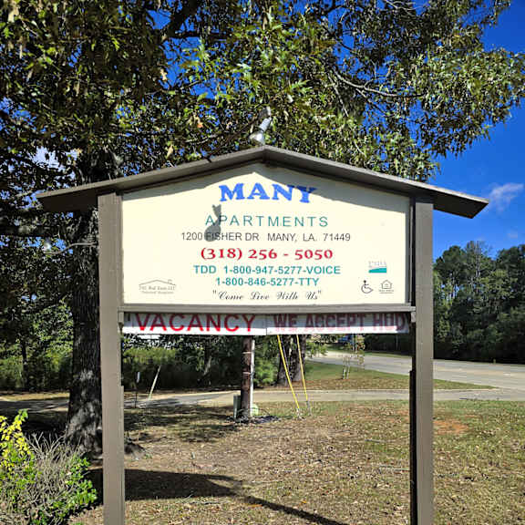 a sign for mant apartments is displayed in front of a tree.